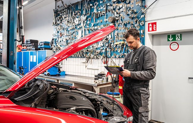 Autohaus Sayler in Ulm Mitarbeiter vor offener Motorhaube füllt Checkliste aus